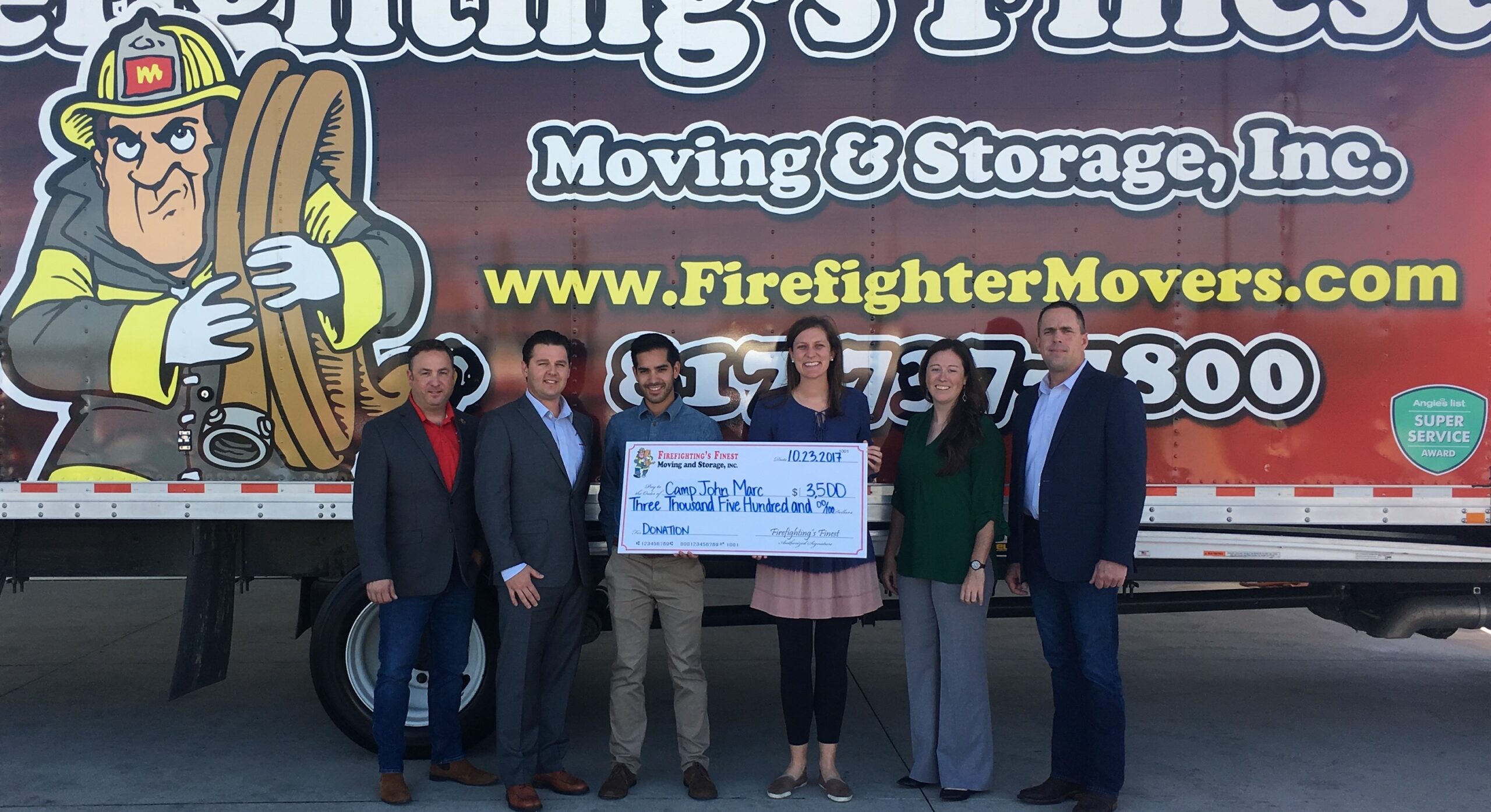 company's leadership team presenting donation check in front of moving truck